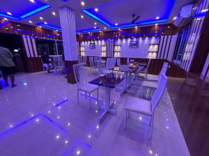 un comedor con luces púrpuras, mesas y sillas en Bonobithikaloy Resort & Restaurant, en Chālsa Mahābāri