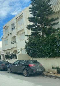 dwa samochody zaparkowane przed budynkiem z drzewem w obiekcie عين زغوان الشمالية المرسي w mieście La Marsa
