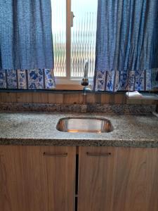 a sink in a kitchen with a window with blue curtains at Mini casa Contêiner em Bombas in Bombinhas