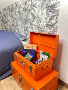 uma mala laranja com livros em cima ao lado de uma cama em Le charme Dubois em Dijon