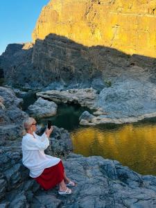 uma mulher sentada numa rocha a tirar uma foto da água em Wadi Al Arbeieen Resort em Mascate