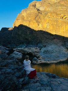 Eine Person, die auf Felsen in der Nähe des Wassers sitzt in der Unterkunft Wadi Al Arbeieen Resort in Muscat