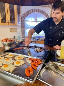 un hombre cocinando huevos y salchichas en una parrilla en Hotel Podlesí en Podlesí