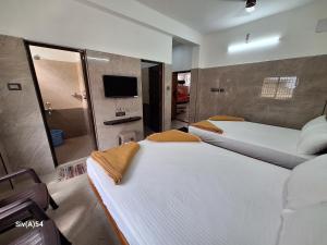two beds in a room with a tv and a bathroom at Viruksham Residency in Palani