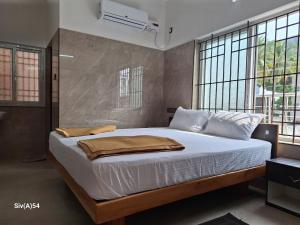 a bedroom with a bed with white sheets and windows at Viruksham Residency in Palani