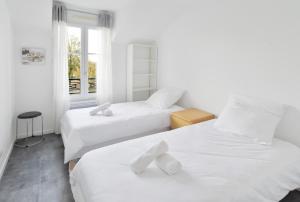 two beds in a white room with a window at L'Amandier Disneyland JO Paris 2024 pour 4 personnes et 1 bébé in Bailly-Romainvilliers