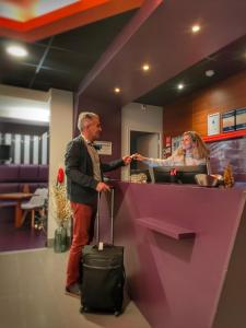 a man with a suitcase standing at a counter with a woman at Best Western Hotel De Paris in Laval