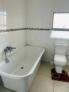 a white bathroom with a tub and a toilet at Cozy Farm 3BDRM 8 km ThabaBosiu in Maseru