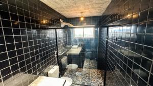 Baño de azulejos negros con aseo y lavamanos en Casa Concept, en Mucugê