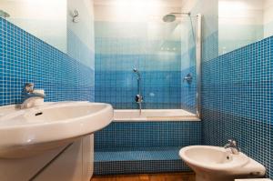 W wyłożonej niebieskimi kafelkami łazience znajduje się umywalka i wanna. w obiekcie Vittore Rooms & Apartment w Mediolanie