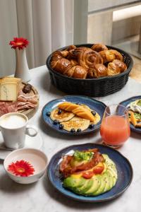 einen Tisch mit Teller mit Lebensmitteln und einen Korb mit Brot in der Unterkunft Hotel Le Place d'Armes - Relais & Châteaux in Luxemburg (Stadt)