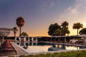 a large swimming pool with chairs and palm trees at Grande Real Villa Itália Hotel & Spa in Cascais