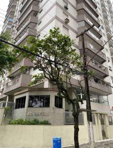 wysoki budynek z drzewem przed nim w obiekcie Apartamento a 100m. da Praia de Pitangueiras w mieście Guarujá