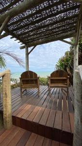 dos bancos sentados en una terraza de madera con la playa en Pousada Flor Do Mar en Caraíva