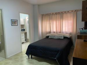 1 dormitorio con 1 cama con edredón negro y ventana en Departamento frente al Mar Necochea en Necochea