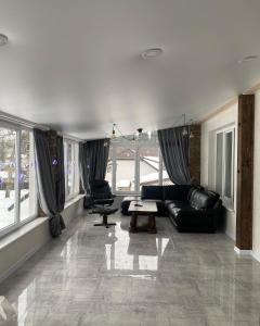 a living room with black leather furniture and large windows at Котедж Смерекова хата- Пилипець in Kelechin