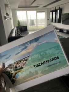 a person holding a book in a living room at Green Penthouse in Tiszaújváros