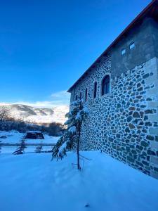 Peshkopi的住宿－Bujtina Oxhaku i Docit，雪中有一棵树的石头建筑