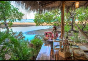 a woman sitting at a table near the beach at Ocho Artisan Bungalows in Tamarindo