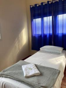 a bedroom with two beds and a window with blue curtains at Pousada Família Guarapari in Guarapari