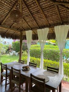 a table and chairs under a thatched roof at Casa Jasmim Imbassaí-BA in Mata de Sao Joao