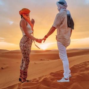mężczyzna i kobieta stojący na pustyni trzymając się za ręce w obiekcie Rihanna Desert Camp w mieście Merzouga