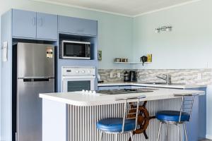 a kitchen with a counter with two blue bar stools at Calypso Cottage, Bright bach, Water view in Raglan