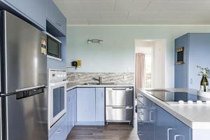 uma cozinha com armários azuis e um frigorífico de aço inoxidável em Calypso Cottage em Raglan