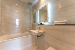 W łazience znajduje się umywalka, wanna i lustro. w obiekcie Oatlands Park Hotel w mieście Weybridge