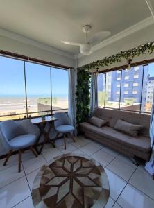 a living room with a couch and a table and windows at Apto 2 dorm com vista para o mar in Capão da Canoa