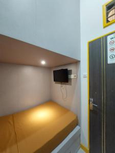 a small bed in a small room with a tv at Autumn Living Hotel in Surabaya