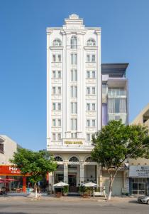 a tall white building with trees in front of it at Titan Hotel Da Nang in Da Nang