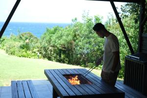 Ein Mann kocht über einem Feuer auf einem Picknicktisch in der Unterkunft Monterey House by SANA in Tateyama