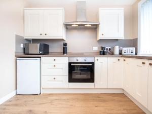 uma cozinha branca com armários e electrodomésticos brancos em Colbheinn Cottage em Brora