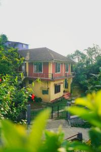 ein gelbes und rotes Haus mit einem Zaun und Bäumen in der Unterkunft Eshwari Cottage in Madikeri