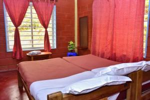 a bedroom with a bed with red curtains and a window at Eshwari Cottage in Madikeri