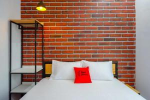 - un oreiller rouge sur un lit en face d'un mur de briques dans l'établissement RedDoorz near Universitas Muhammadiyah Purwokerto 2, à Kembaran