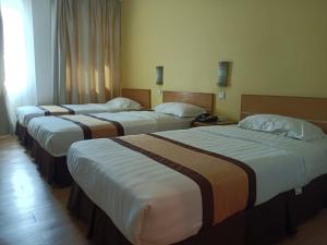 a row of four beds in a hotel room at Tang Dynasty Lodge Tuaran in Tuaran