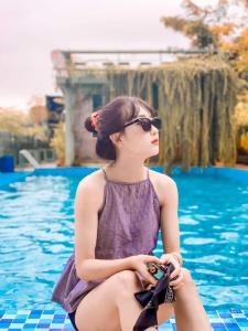 une femme en lunettes de soleil assise à côté d'une piscine dans l'établissement Ba Vì Madela, à Ba Vì