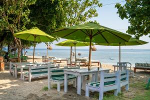eine Gruppe von Tischen und Stühlen mit Sonnenschirmen am Strand in der Unterkunft Taman Sari Bali Resort and Spa in Pemuteran
