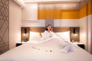 a woman sitting on a bed talking on a cell phone at Madi Paidi Bangkok, Autograph Collection in Bangkok