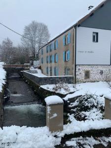 a building with snow on the ground next to a river at Gîte Au Creux Du Moulin in Bussang