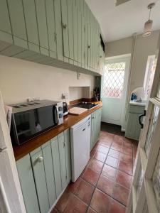 een keuken met groene kasten en een magnetron bij Cosy Countryside Cottage - Hot Tub & Dog friendly in Castle Rising