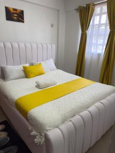 a white bed with a yellow and white blanket at Serene 2 Bedrooms Apartment in Kericho