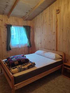uma cama num quarto de madeira com uma janela em cabaña zoila em Coñaripe