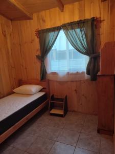 um pequeno quarto com uma cama e uma janela em cabaña zoila em Coñaripe