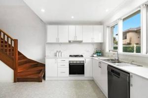 uma cozinha com armários brancos, um lavatório e uma escadaria em Delightful Home with Amazing city views! em Sydney