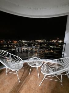three white chairs on a balcony with a view of a city at Departamento Boulevard con cochera in Santa Fe