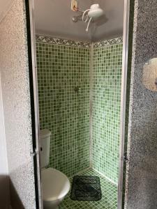 a bathroom with a toilet and a shower with green tiles at POUSADA CASA DA FÉ in Aparecida