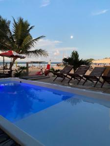 a blue swimming pool with chairs and a beach at POUSADA GENIPABU PRAIA in Extremóz